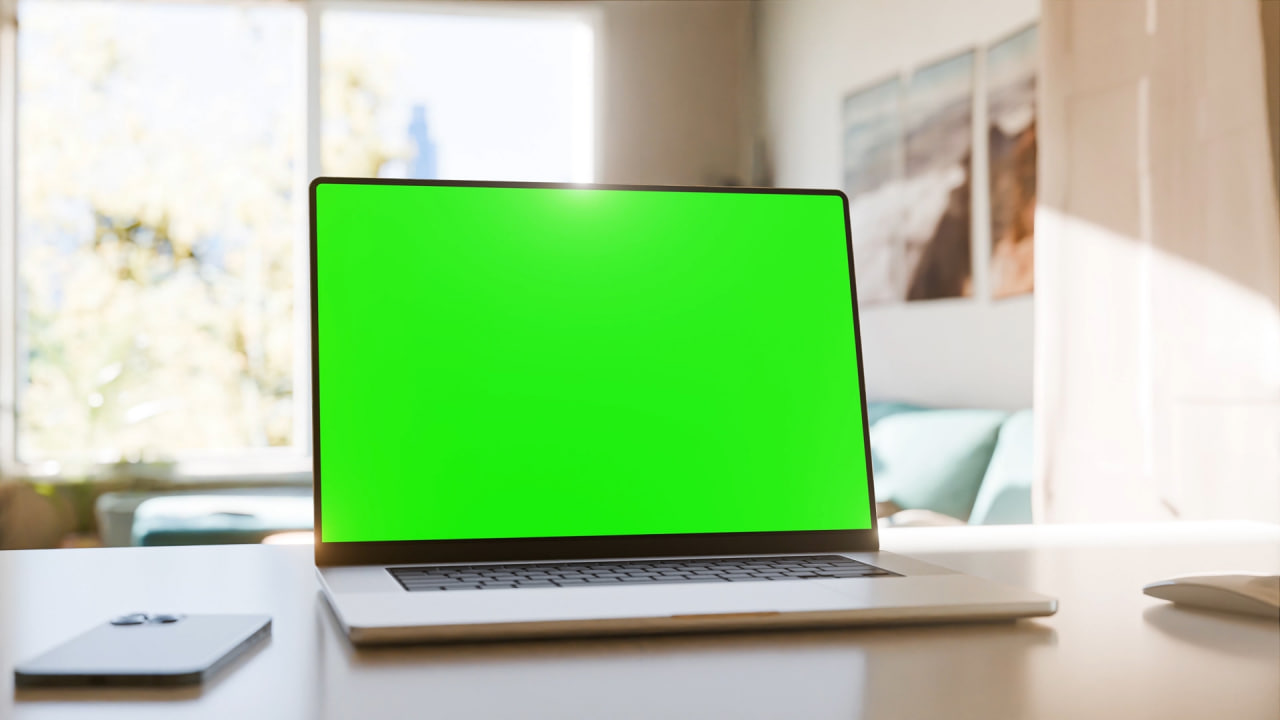 فوتیج لپتاپی با صفحه نمایش سبز روی میز در یک دفتر کار خانگی روشن. ایدهآل برای قرار دادن محتوای خودتان. دوربین دور صفحه میچرخد. فیلم شامل یک لایه ردیابی و یک لایه لوما مت است. ویدیوی استوک