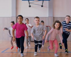 گروهی از دانش‌آموزان ابتدایی که در کلاس درس در سالن ورزشی مدرسه می‌دوند. ویدیوی استوک