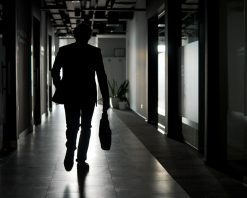 نمای عقب. سیلوئت یک تاجر با کت و شلوار در امتداد راهروی ساختمان اداری امتداد دارد. ویدیوی استوک 4K