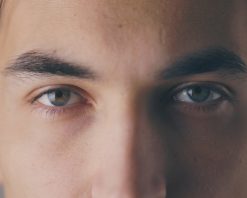 نمای نزدیک از یک مرد جوان آرام که چشمانش را باز می‌کند و به دوربین در دیوار خاکستری پس زمینه در استودیوی 4K نگاه می‌کند، ویدیوی استوک